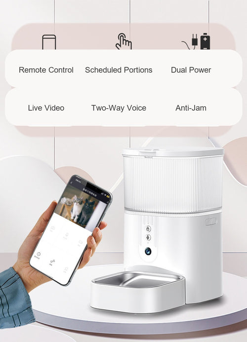 White X42 smart pet feeder with hopper, front camera and stainless bowl, held next to a phone showing live video of a cat