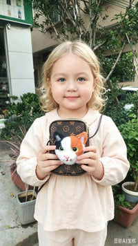 Young girl in a pink dress holding a finished calico cat felt head sculpture against a monogrammed backpack outdoors