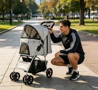 Young man crouching beside the gray pet stroller on a tree-lined path, looking at the pet inside